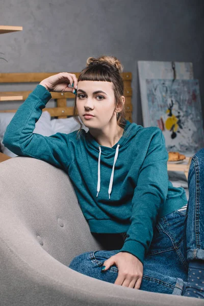 Serious girl sitting on armchair in bedroom and looking at camera — Stock Photo