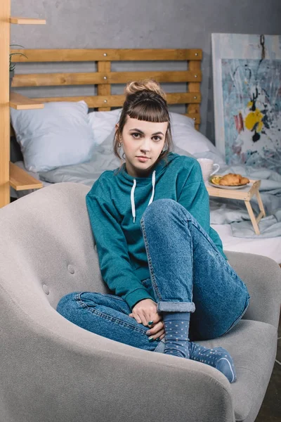 Mädchen sitzt auf Sessel im Schlafzimmer und blickt in Kamera — Stockfoto