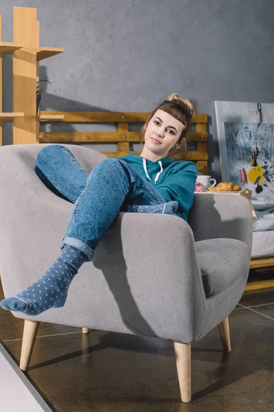 Girl sitting on armchair in bedroom and looking at camera — Stock Photo