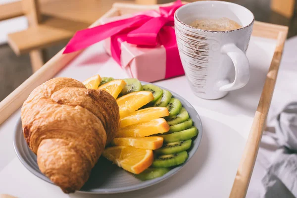 Tablett mit Croissant und Obst und Geschenkbox auf dem Bett — Stockfoto