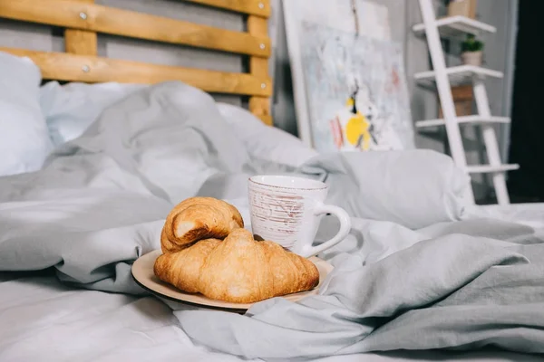 Tasse Kaffee und Croissants auf dem Teller im Bett — Stockfoto