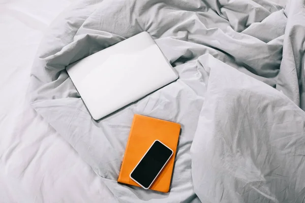 High angle view of laptop with notebook and smartphone on blanket in bedroom — Stock Photo