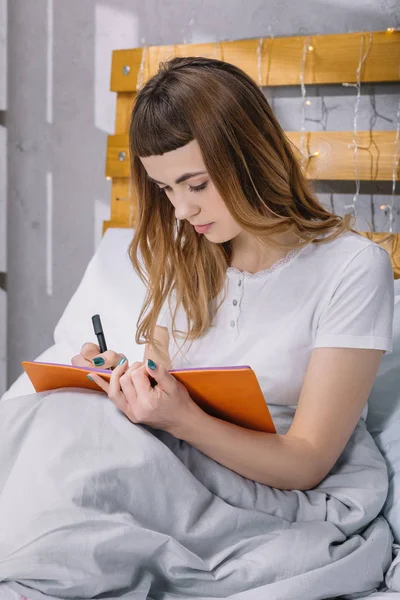 Mädchen schreibt morgens im Bett etwas auf Notizbuch — Stockfoto
