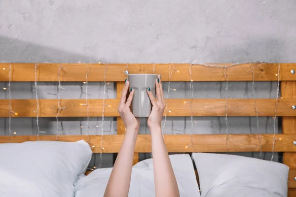 Imagem cortada de menina segurando xícara de café nas mãos e deitado na cama — Fotografia de Stock