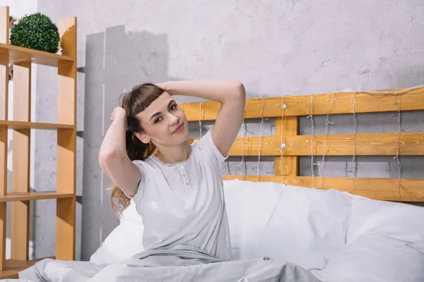 Chica feliz estiramiento en la cama por la mañana y mirando a la cámara - foto de stock