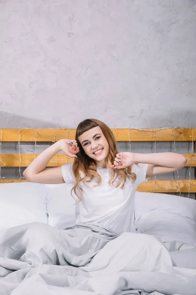 Happy girl stretching in bed in morning and looking at camera — Stock Photo