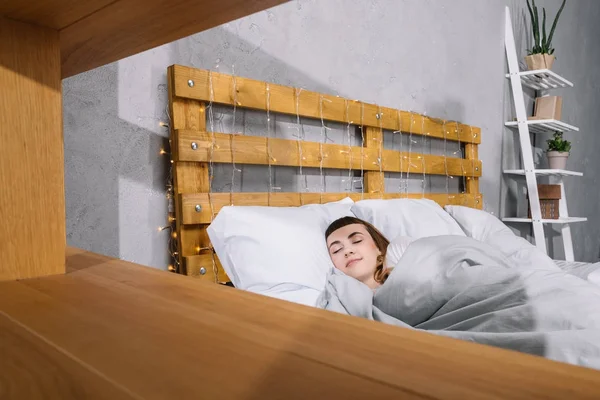 Vista a través de estantes en chica durmiendo en almohadas blancas en el dormitorio - foto de stock