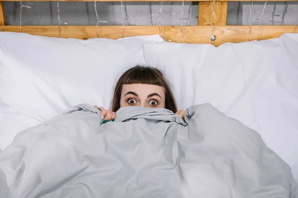 Menina surpreso olhando para fora do cobertor no quarto — Fotografia de Stock