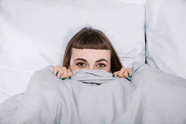 Menina olhando para fora de cobertor no quarto — Fotografia de Stock
