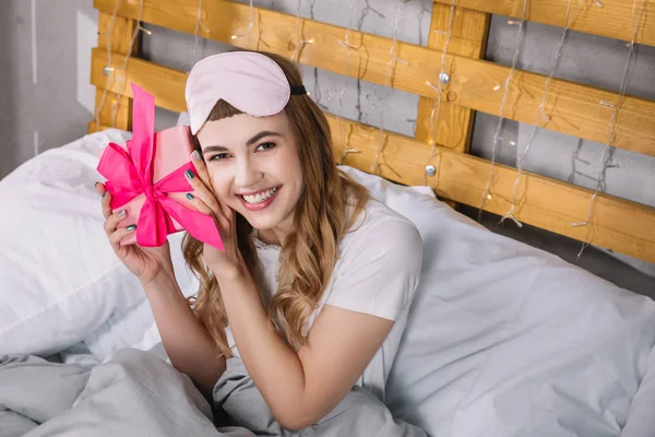 Happy girl sitting in bed and listening what inside present box — Stock Photo