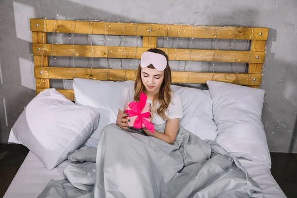 Happy girl sitting in bed with present box — Stock Photo