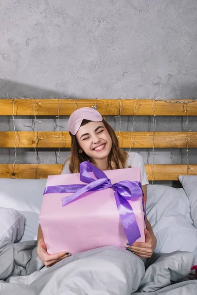 Feliz chica sonriente sentada en la cama con caja presente - foto de stock