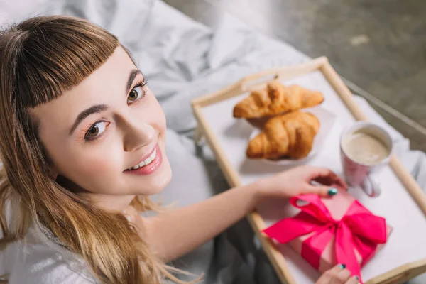 Overhead view of happy girl holding gift box in bed — Stock Photo