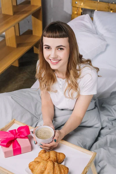 Overhead view of smiling girl holding cup of coffee in bed — Stock Photo