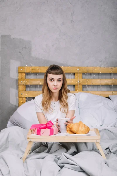 Дівчина сидить у ліжку вранці з кавою і подарунковою коробкою — стокове фото