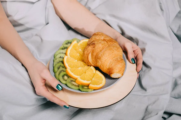 Abgeschnittenes Bild eines Mädchens, das einen Teller mit Früchten und Croissant hält — Stockfoto