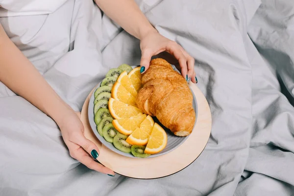 Imagem cortada de menina tomando croissant da placa na cama — Fotografia de Stock