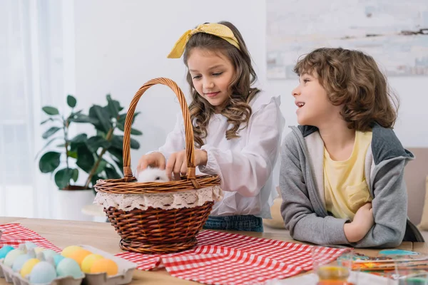 Adorable little kids playing with cute rabbit in basket on table with easter eggs — Stock Photo