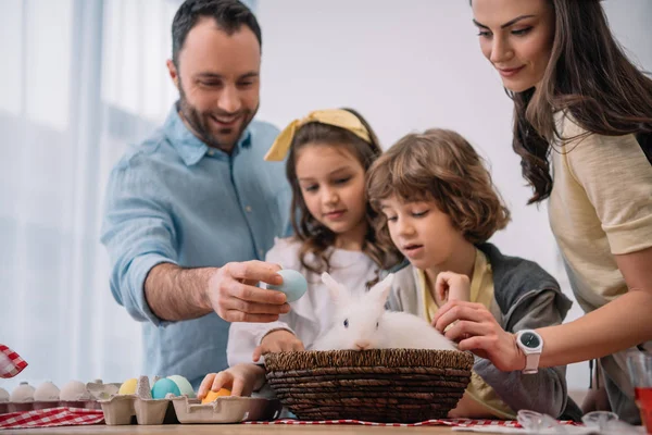 Familia joven preparándose para las vacaciones de Pascua con conejo sentado en la mesa - foto de stock