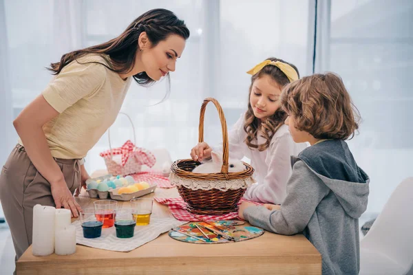 Bambini e mamma che giocano con coniglio pasquale a casa sul tavolo — Foto stock