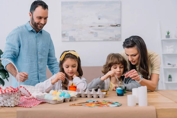 Hermosa familia joven pintando huevos para pascua en casa - foto de stock
