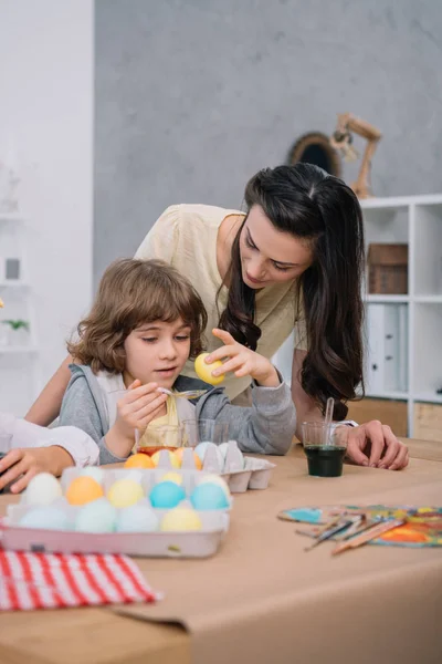 Pequeño hijo ayudando a la madre con huevos pintura para las vacaciones de Pascua - foto de stock