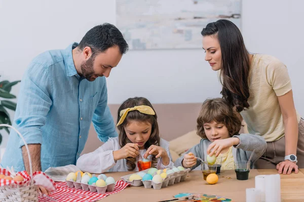 Feliz familia joven pintando huevos para pascua en casa - foto de stock