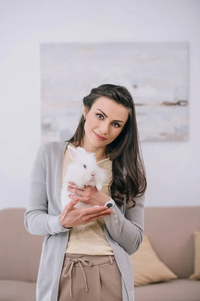 Attractive woman holding white rabbit and looking at camera indoors — Stock Photo