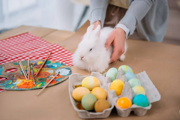 Frau mit weißem Kaninchen auf Tisch mit bunten Ostereiern — Stockfoto