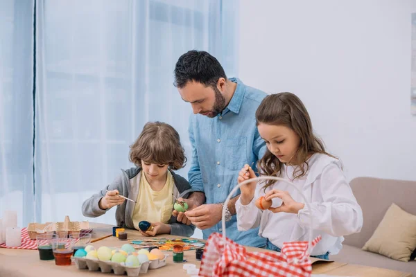 Jeune père et enfants peignant des œufs pour les vacances de Pâques — Photo de stock