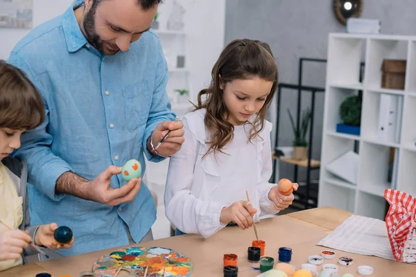 Padre e hijos pintando huevos para las vacaciones de Pascua - foto de stock