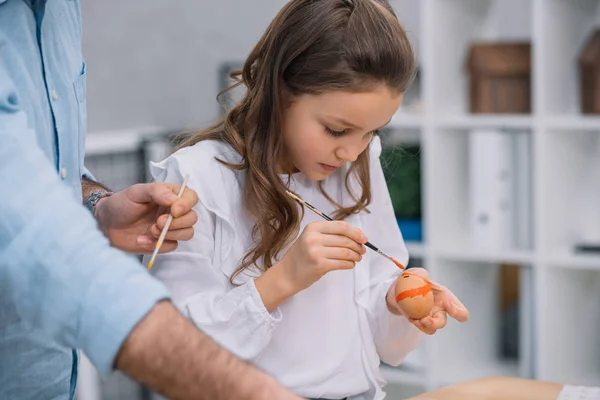 Beautiful little daughter painting easter eggs with father — Stock Photo