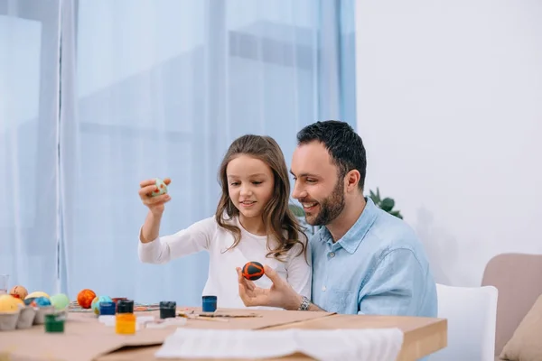 Счастливый молодой отец рисует пасхальные яйца с дочерью — стоковое фото