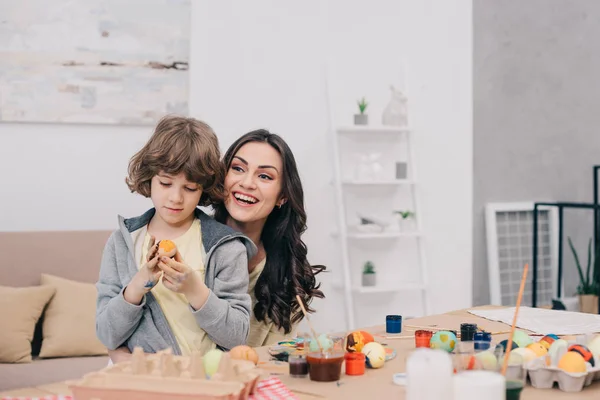 Happy young mother and son painting easter eggs together at home — Stock Photo