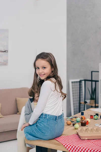 Little child sitting on table at home with easter eggs on it — Stock Photo