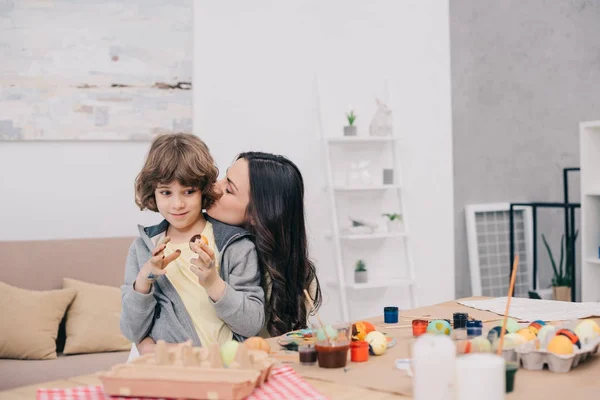 Mother kissing her son while he painting easter eggs — Stock Photo