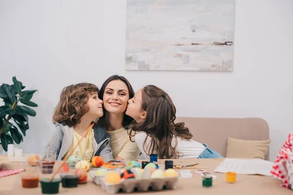 Kids kissing mother while painting easter eggs — Stock Photo