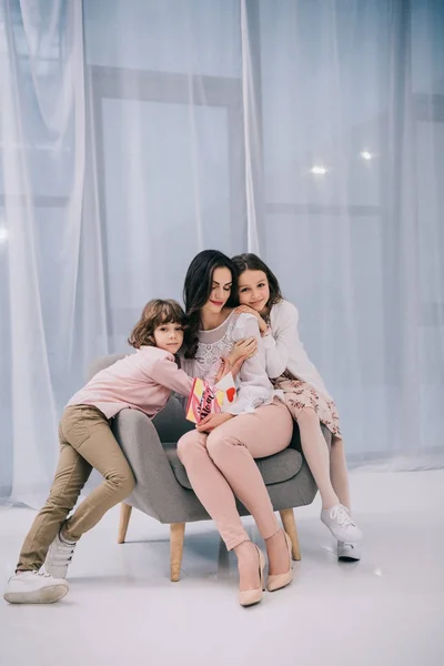Kinder umarmen sich mit Mutter, während sie am Muttertag zusammen auf der Couch sitzen — Stockfoto