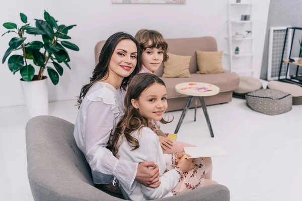 Kinder überreichen Mutter Glückwunschkarten zum Muttertag, während sie gemeinsam im Sessel sitzen — Stockfoto