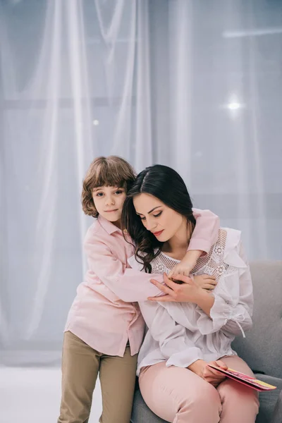 Filho abraçando a mãe em casa enquanto ela se senta em poltrona, conceito dia mães — Fotografia de Stock