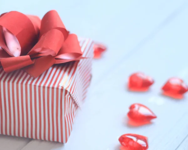 Geschenkbox mit roter Schleife und Herzen auf hellem Hintergrund — Stockfoto