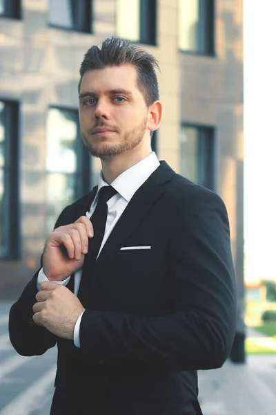 Hombre de negocios ajustando su corbata en la entrada del edificio de oficinas — Foto de Stock