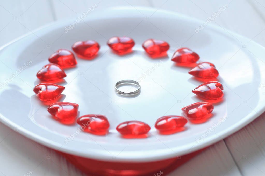 close up.ring and red hearts on a white plate