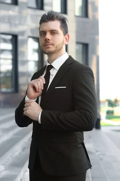 Empresário ajustando sua gravata na entrada do prédio de escritórios — Fotografia de Stock