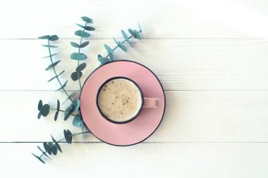 Beyaz desenli bir masada bir fincan sade kahve ve okaliptüs dalı. Üst görünüm, minimalizm biçimi, kopyalama alanı.