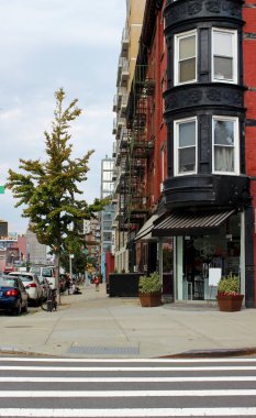 Pencereli kırmızı bir evin siyah cjrner cephesi. Yangın merdivenleri olan Clfssic Amerikan evleri. Dükkanları ve kuaförleri olan bir sokak. Sokak, Brooklyn, New York.