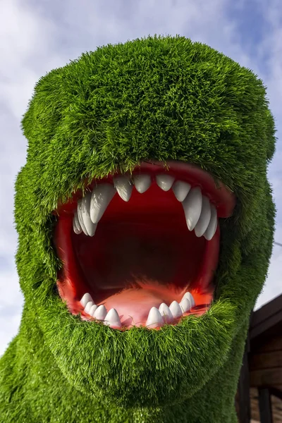 Tyrannosaurus head wuth open mouth covered with artificial green grass