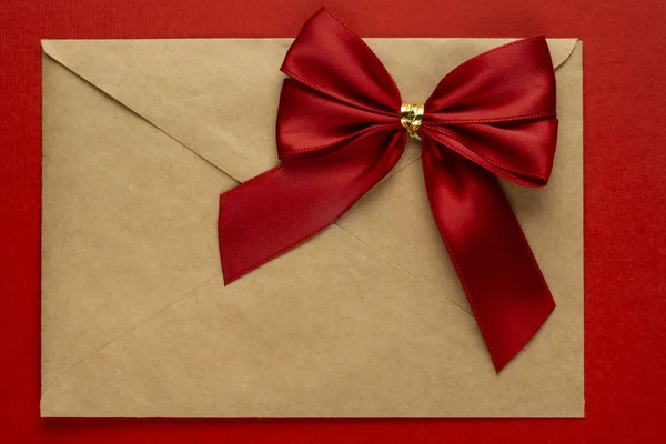 Gift red bow on a craft envelope on textured red background