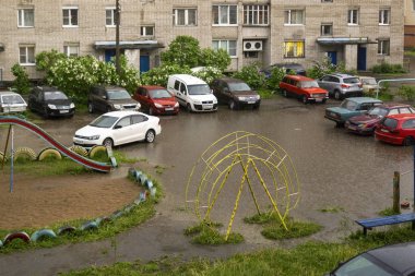 Şehir avlusundaki arabalar yaz yağmuru sırasında oyun parkındaki su birikintilerinde duruyor.