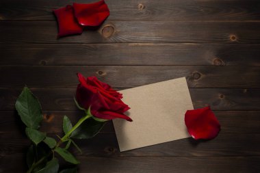 Boş kart, kırmızı gül yaprakları ve kırsal ahşap arka planda kırmızı gül çiçeği